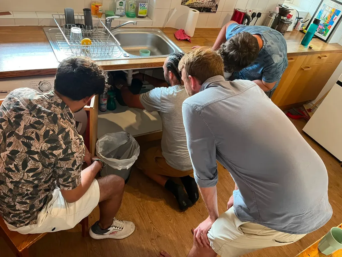 Group of four learning plumbing basics around a kitchen sink at a hands-on DIY workshop in London